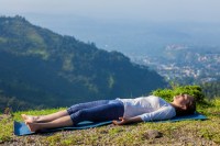 54728563 - woman relaxes in yoga asana savasana - corpse pose outdoors in himalayas. himachal pradesh, india